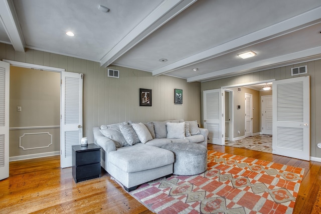 living room featuring visible vents, beam ceiling, baseboards, and light wood finished floors