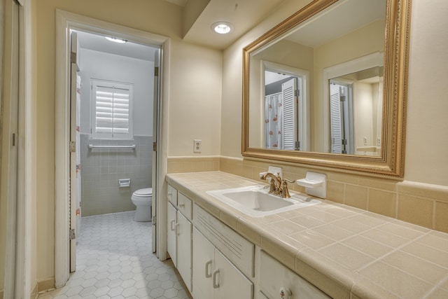 bathroom with a wainscoted wall, toilet, tile walls, tile patterned flooring, and vanity