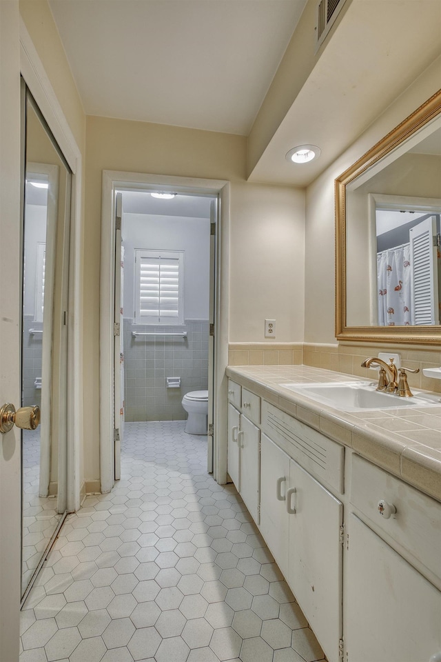 full bath featuring visible vents, a wainscoted wall, toilet, vanity, and tile walls