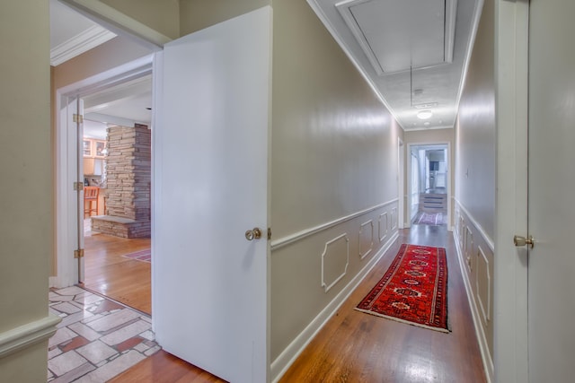 hallway with ornamental molding, wood finished floors, wainscoting, a decorative wall, and attic access