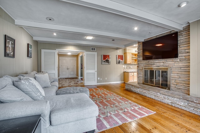 living area featuring visible vents, beam ceiling, light wood-style flooring, a fireplace, and baseboards