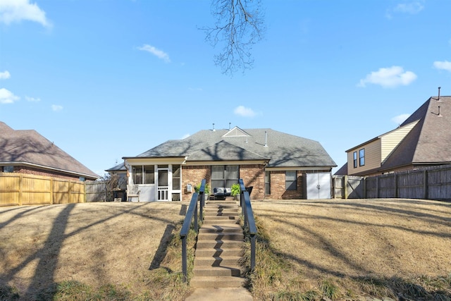 view of front of property featuring a front yard, stairway, a fenced backyard, a sunroom, and brick siding