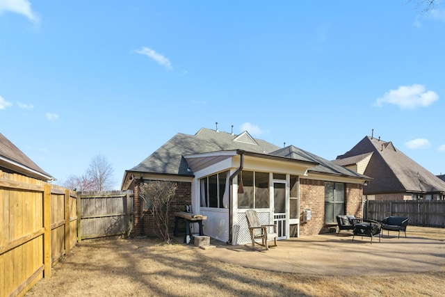 rear view of property featuring brick siding, roof with shingles, a fenced backyard, a sunroom, and a patio