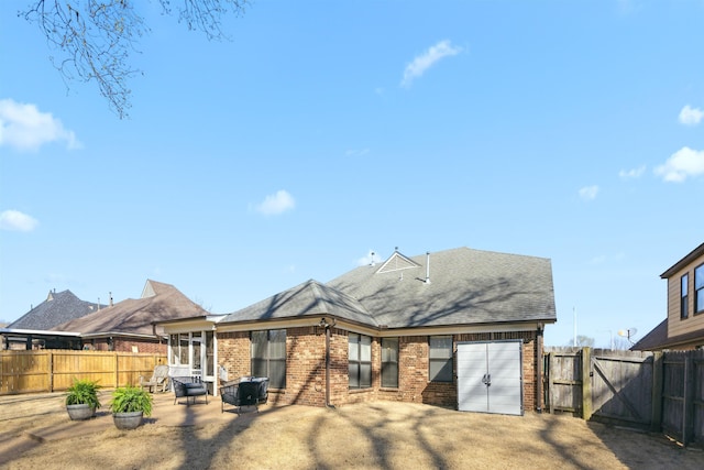 rear view of house with a gate, a fenced backyard, a garage, a patio area, and brick siding