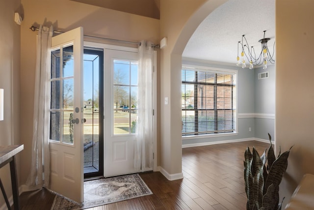 foyer featuring visible vents, arched walkways, baseboards, and dark wood-style flooring