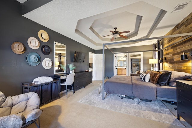 carpeted bedroom featuring visible vents, ensuite bath, wood walls, a raised ceiling, and ceiling fan