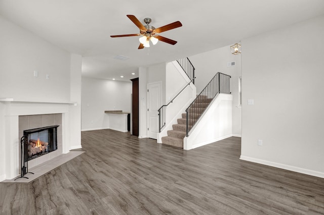 unfurnished living room featuring stairway, a fireplace, ceiling fan, and wood finished floors