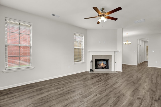 unfurnished living room with visible vents, baseboards, ceiling fan with notable chandelier, a tile fireplace, and wood finished floors