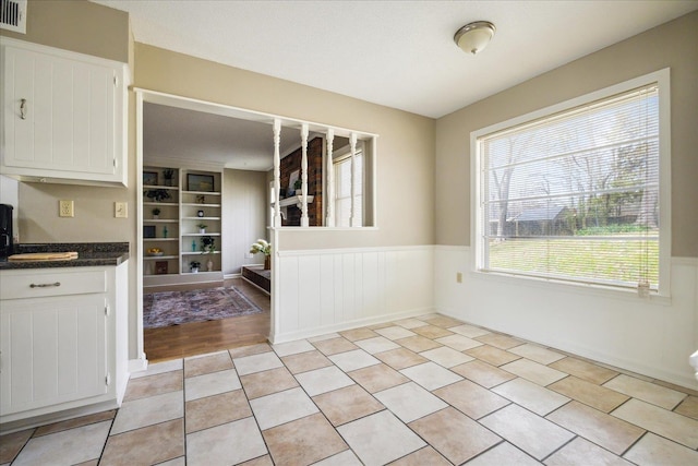 unfurnished dining area featuring light tile patterned floors, visible vents, built in shelves, and wainscoting