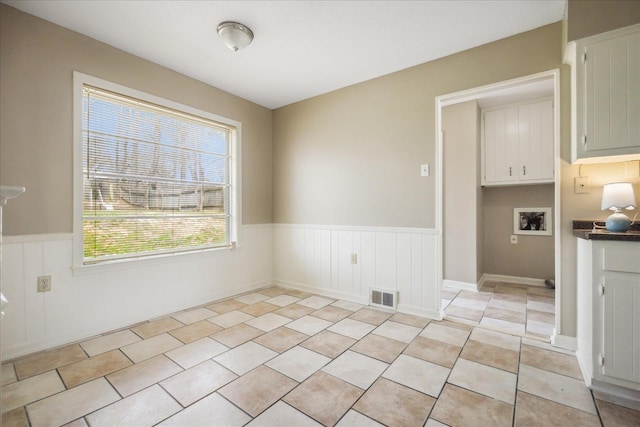 unfurnished dining area with a wainscoted wall, light tile patterned flooring, and visible vents