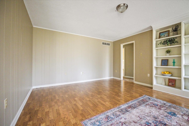 spare room with visible vents, ornamental molding, built in features, and wood finished floors