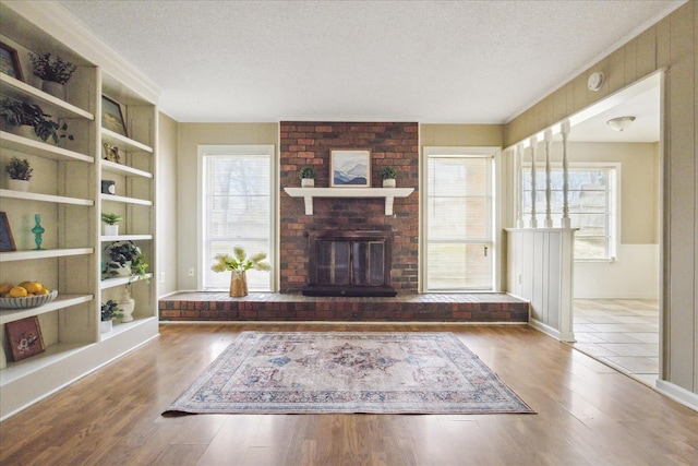 unfurnished living room with a fireplace, a textured ceiling, built in shelves, and wood finished floors