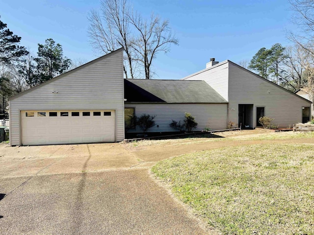 view of side of property featuring a lawn, driveway, a chimney, and a garage