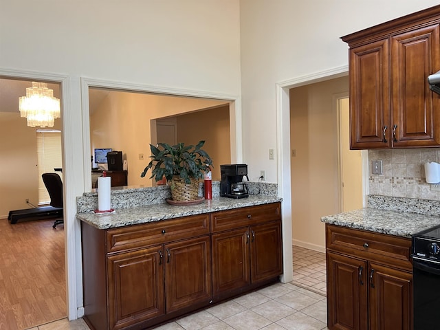 kitchen featuring tasteful backsplash, a notable chandelier, light stone counters, and electric range