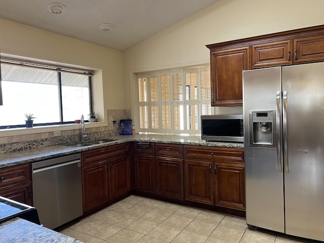 kitchen with a sink, stone countertops, stainless steel appliances, light tile patterned floors, and lofted ceiling