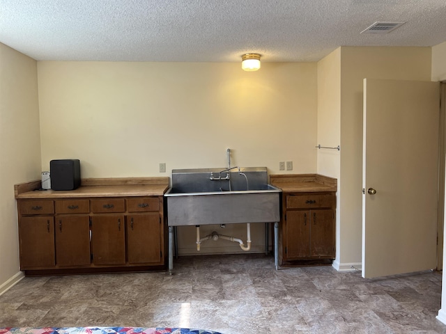 kitchen featuring baseboards, visible vents, a sink, light countertops, and brown cabinets