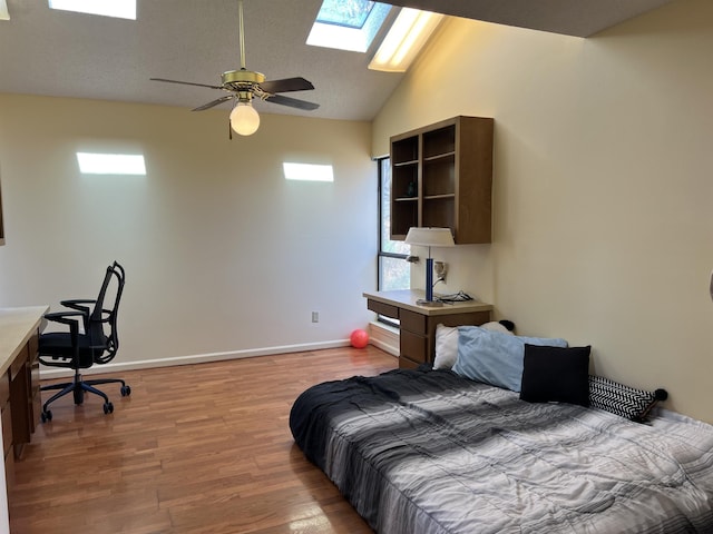 bedroom featuring lofted ceiling with skylight, ceiling fan, light wood-type flooring, and baseboards