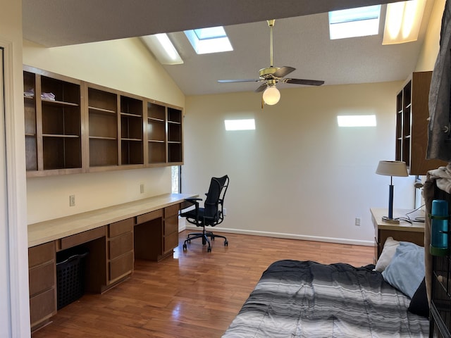 office with vaulted ceiling with skylight, dark wood-type flooring, ceiling fan, and built in desk
