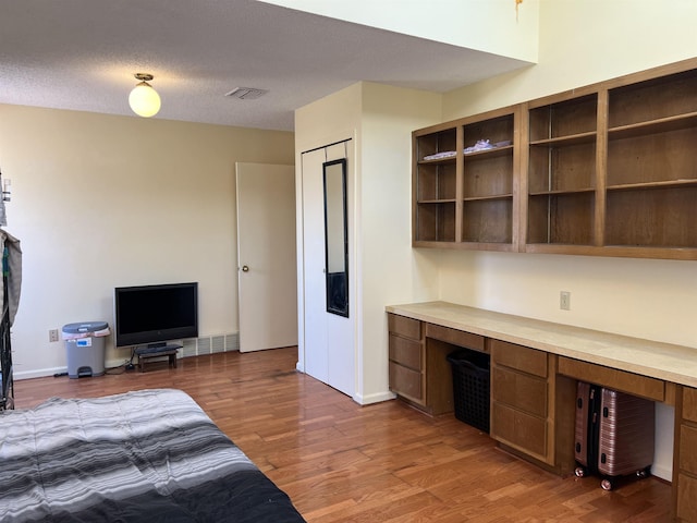 bedroom featuring baseboards, visible vents, built in study area, a textured ceiling, and light wood-type flooring