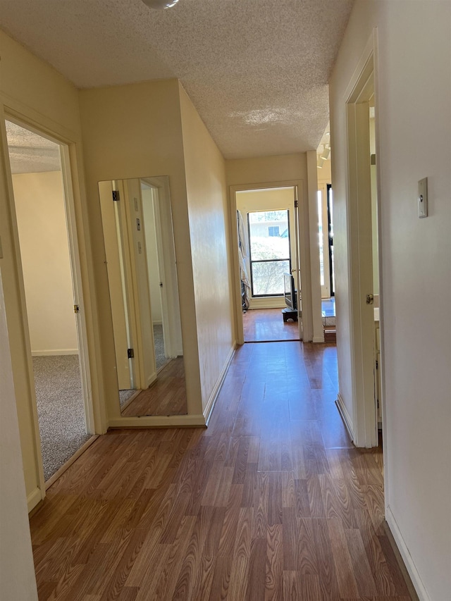 hall featuring baseboards, a textured ceiling, and wood finished floors