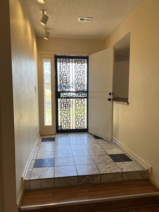 foyer entrance with visible vents, a textured ceiling, and baseboards