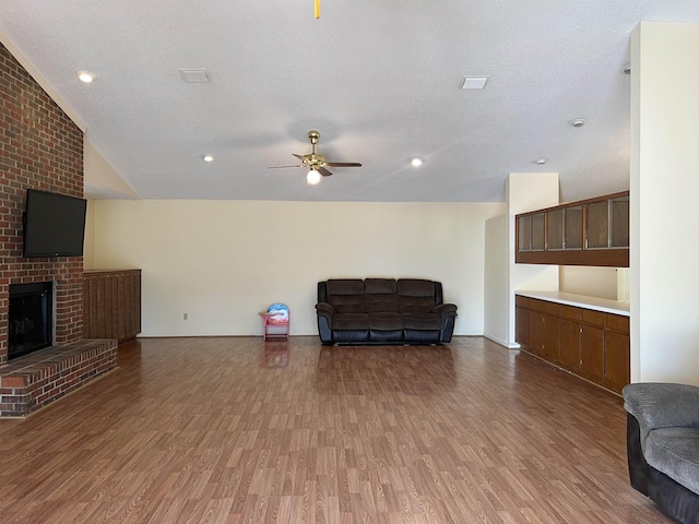 living area with vaulted ceiling, a brick fireplace, wood finished floors, and ceiling fan