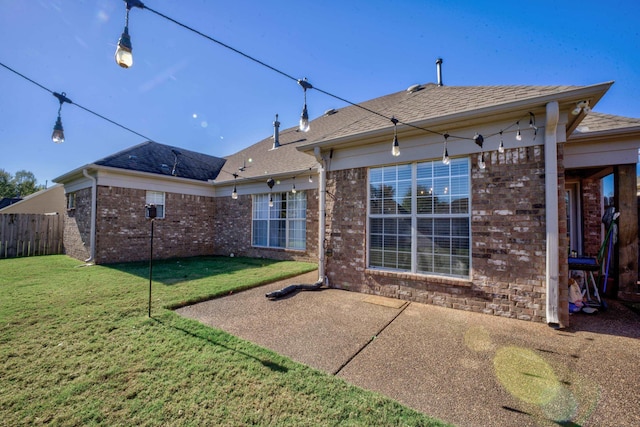 rear view of house with a patio, fence, a yard, a shingled roof, and brick siding