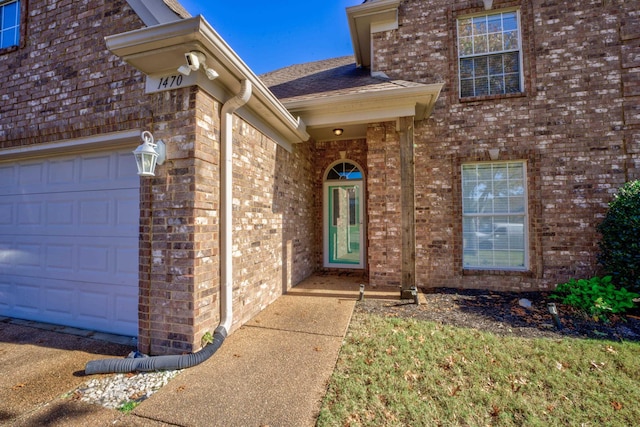 doorway to property featuring brick siding, an attached garage, and roof with shingles