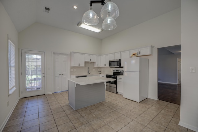 kitchen featuring light tile patterned floors, high vaulted ceiling, a kitchen island, light countertops, and appliances with stainless steel finishes