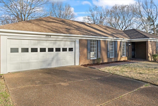 ranch-style house featuring an attached garage, brick siding, and roof with shingles