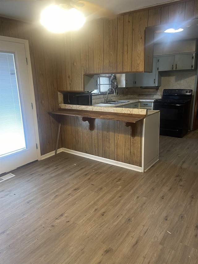 kitchen featuring visible vents, a kitchen bar, black range with electric stovetop, a sink, and wood finished floors