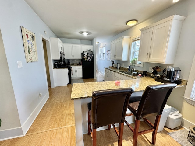 kitchen with a kitchen bar, black appliances, light wood-style flooring, and a peninsula