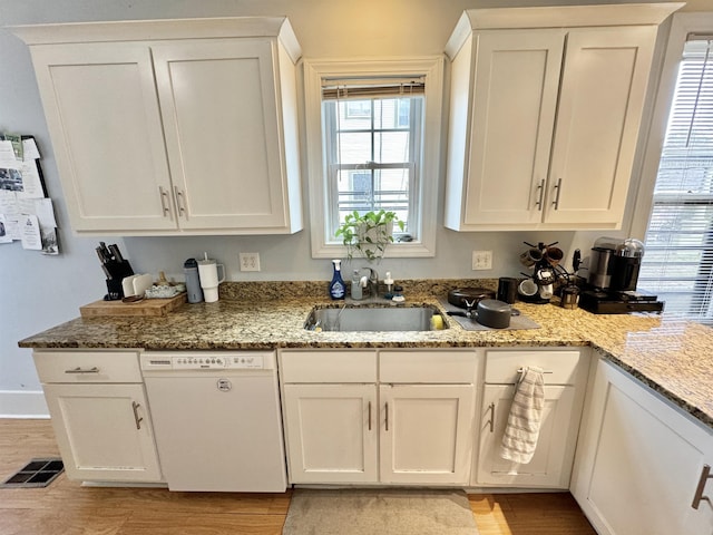 kitchen with dishwasher, light stone counters, light wood-style floors, white cabinets, and a sink