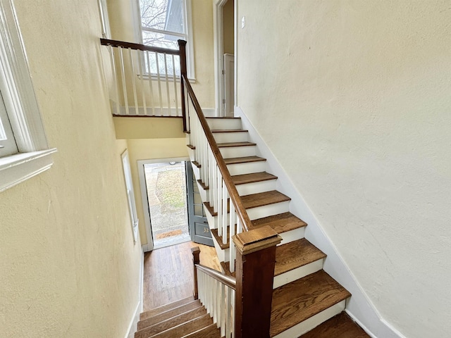 stairs with a healthy amount of sunlight, wood finished floors, and a textured wall