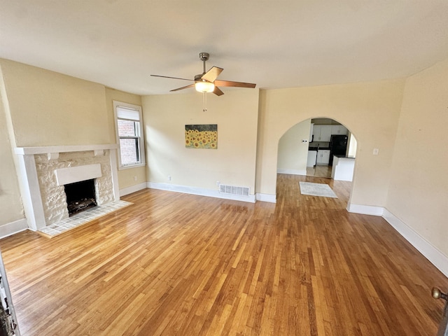 unfurnished living room with light wood-type flooring, visible vents, arched walkways, and ceiling fan
