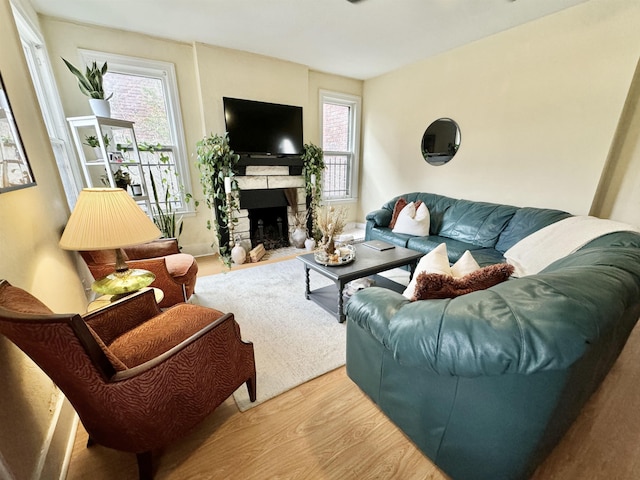 living area featuring a wealth of natural light, a stone fireplace, and wood finished floors