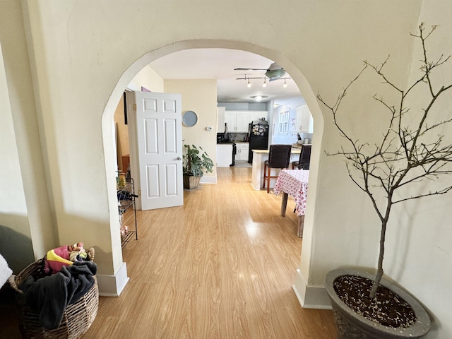 hallway featuring light wood-type flooring, arched walkways, and baseboards