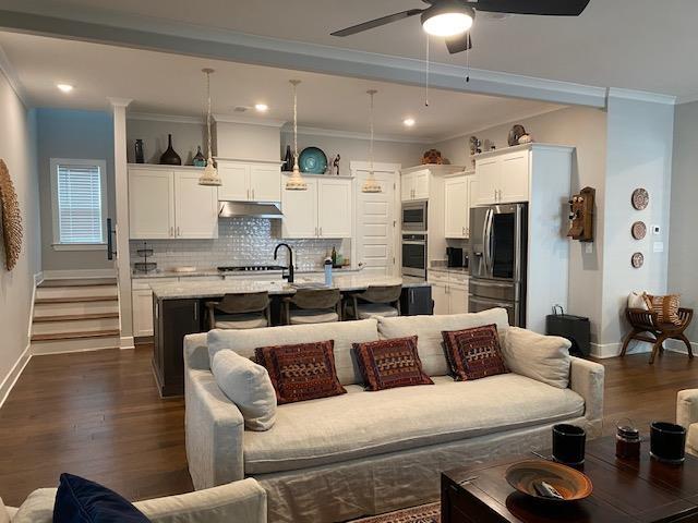 living area featuring dark wood-style floors, baseboards, crown molding, and ceiling fan