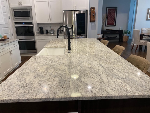 kitchen featuring a large island with sink, light stone counters, appliances with stainless steel finishes, and a sink