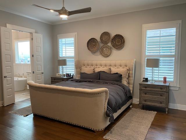 bedroom featuring ensuite bath, multiple windows, baseboards, and dark wood-style flooring