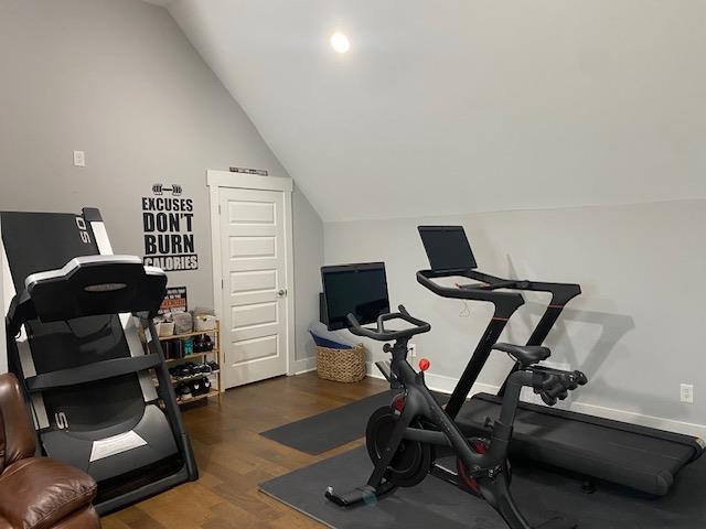 exercise room with baseboards, wood finished floors, and vaulted ceiling