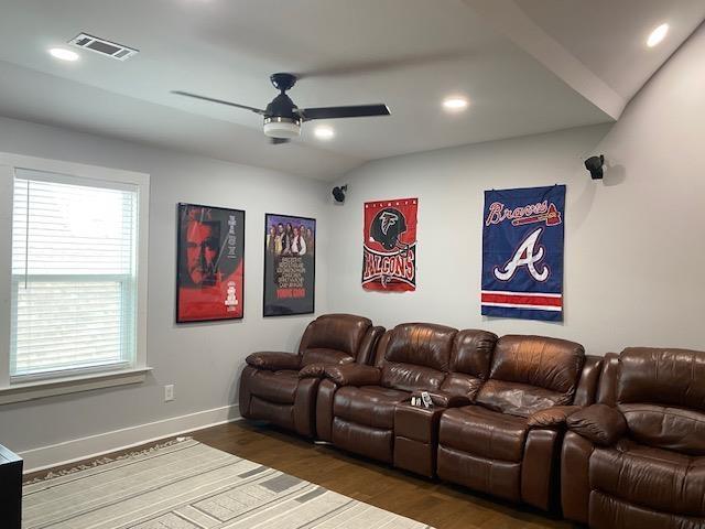 home theater room featuring visible vents, wood finished floors, lofted ceiling, and ceiling fan