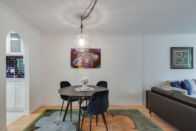 dining area featuring light wood-style flooring, baseboards, arched walkways, and ornamental molding