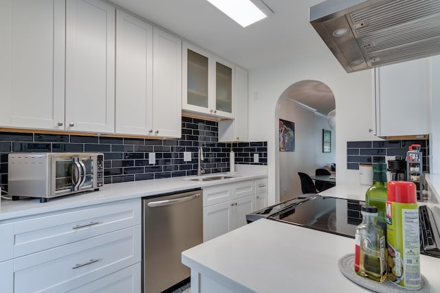 kitchen with ventilation hood, arched walkways, a sink, appliances with stainless steel finishes, and white cabinetry