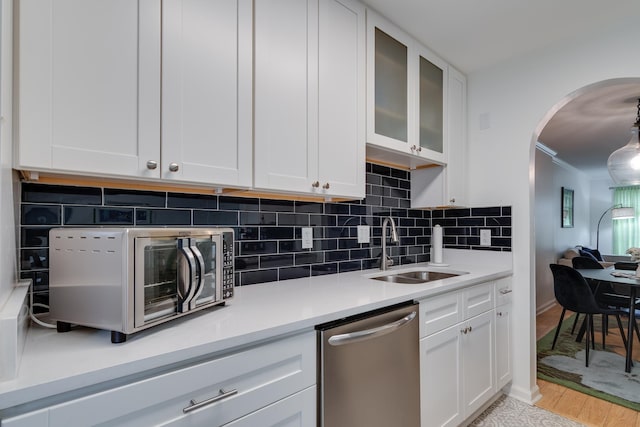 kitchen featuring tasteful backsplash, stainless steel appliances, arched walkways, white cabinetry, and a sink