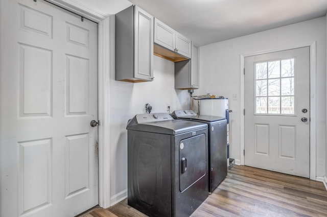 laundry area with washing machine and clothes dryer, cabinet space, light wood finished floors, and water heater