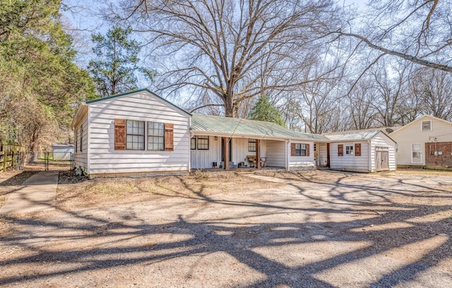 view of front of house with fence, driveway, covered porch, board and batten siding, and metal roof