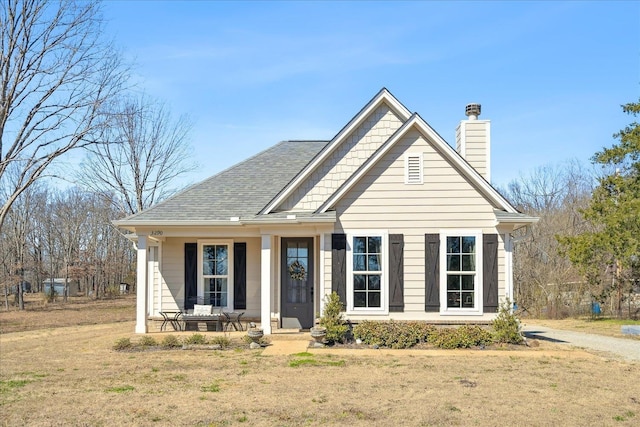 view of front of property with a shingled roof, a porch, a front lawn, and a chimney