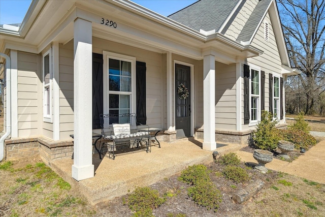 property entrance featuring covered porch and a shingled roof