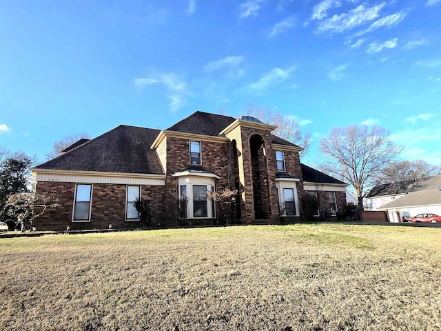 traditional home with brick siding, a front lawn, and roof with shingles